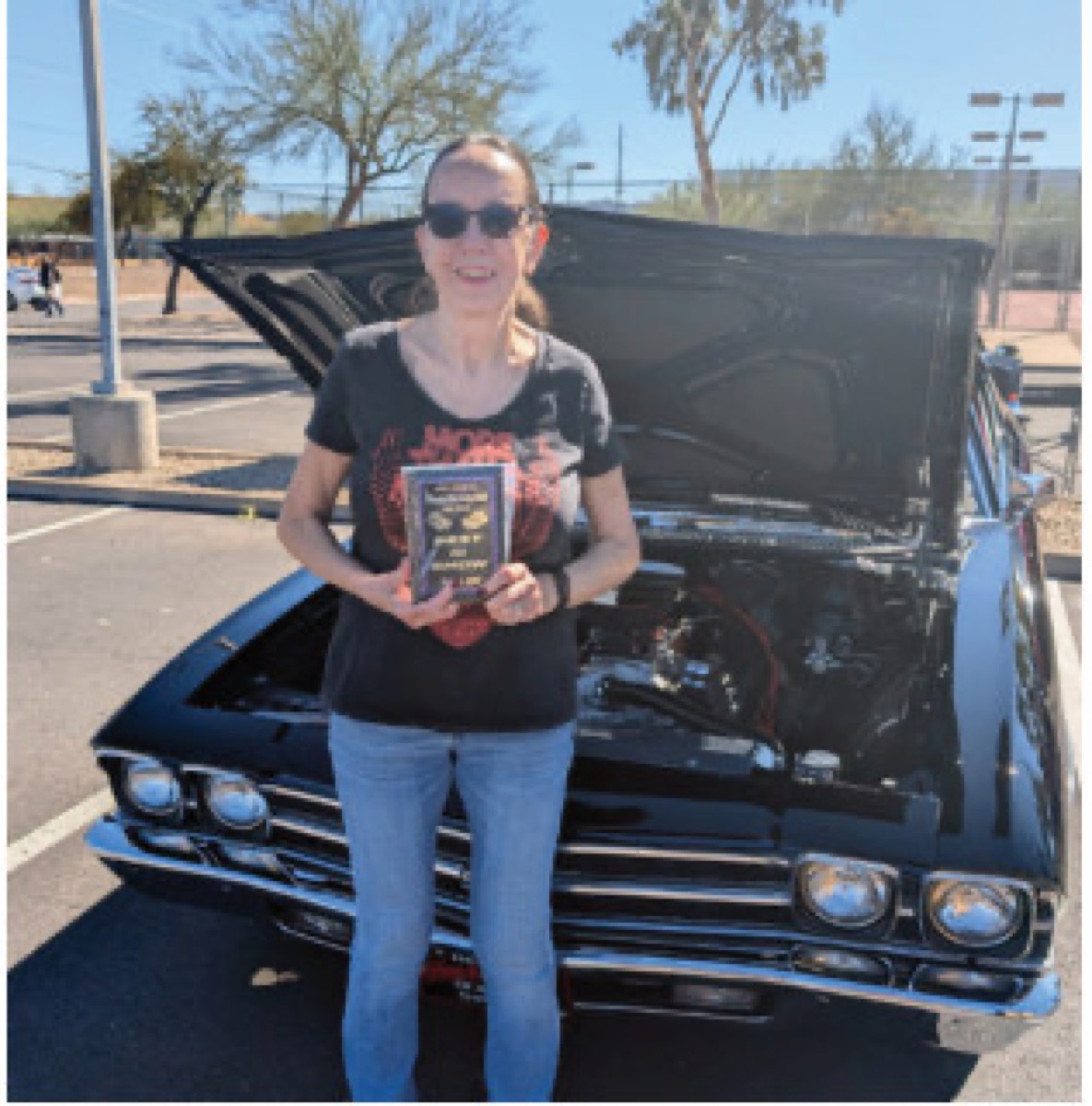 A Best in Show winner holding her plaque in front of a classic muscle car